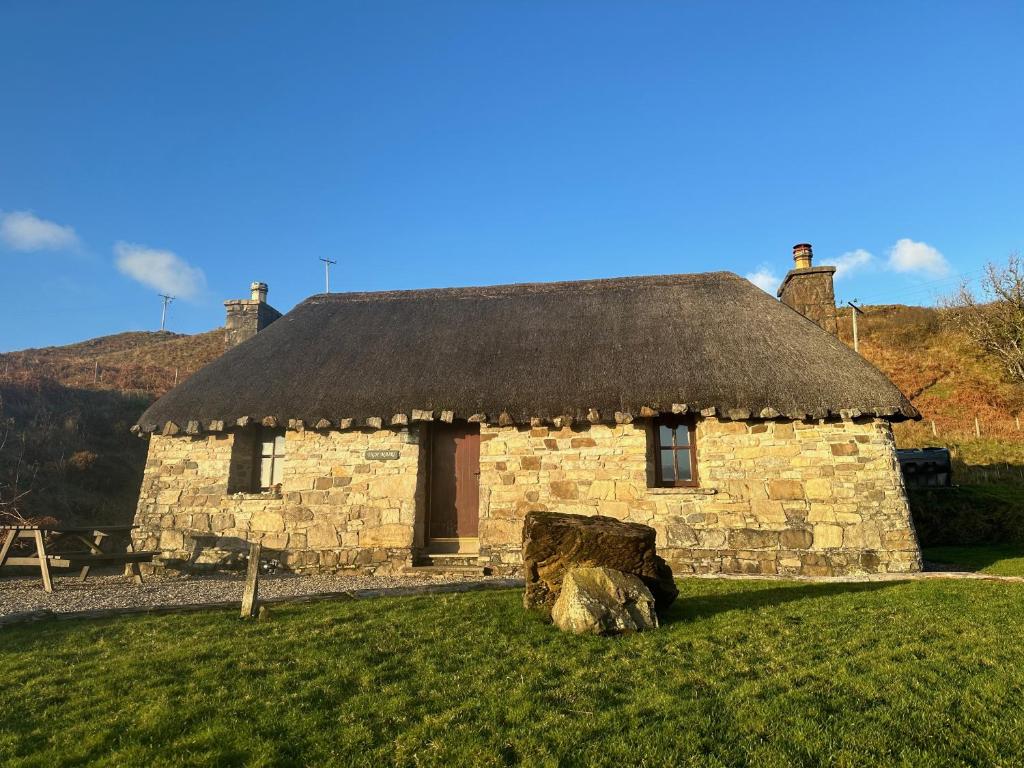 a stone house with a thatched roof on a field at Tigh Mairi at Mary's Thatched Cottages in Elgol