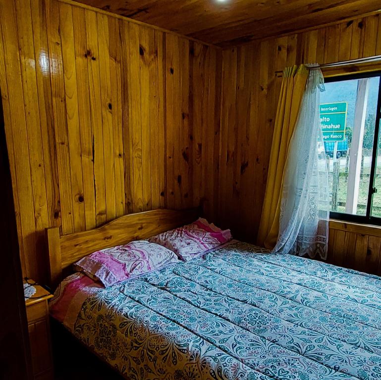 Cama en habitación de madera con ventana en Acogedora Cabaña, en Riñinahue