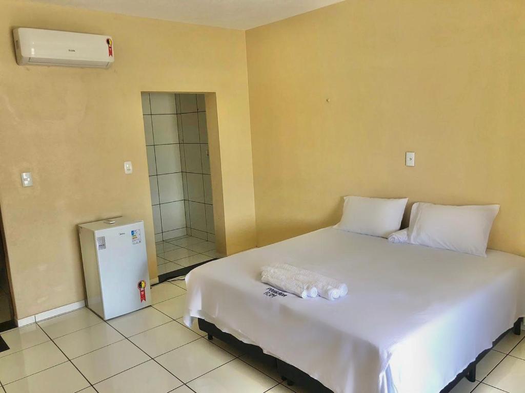 1 dormitorio con cama blanca y nevera pequeña en Pousada B3M en Itarema