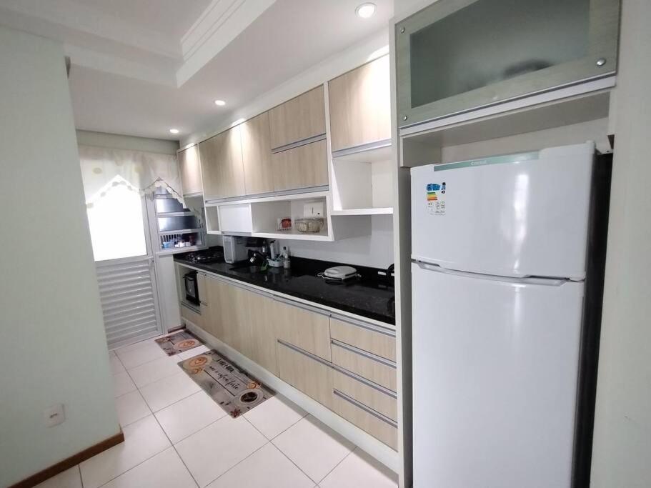 uma cozinha com armários brancos e um frigorífico branco em Apartamento 2 quartos na praia em Florianópolis