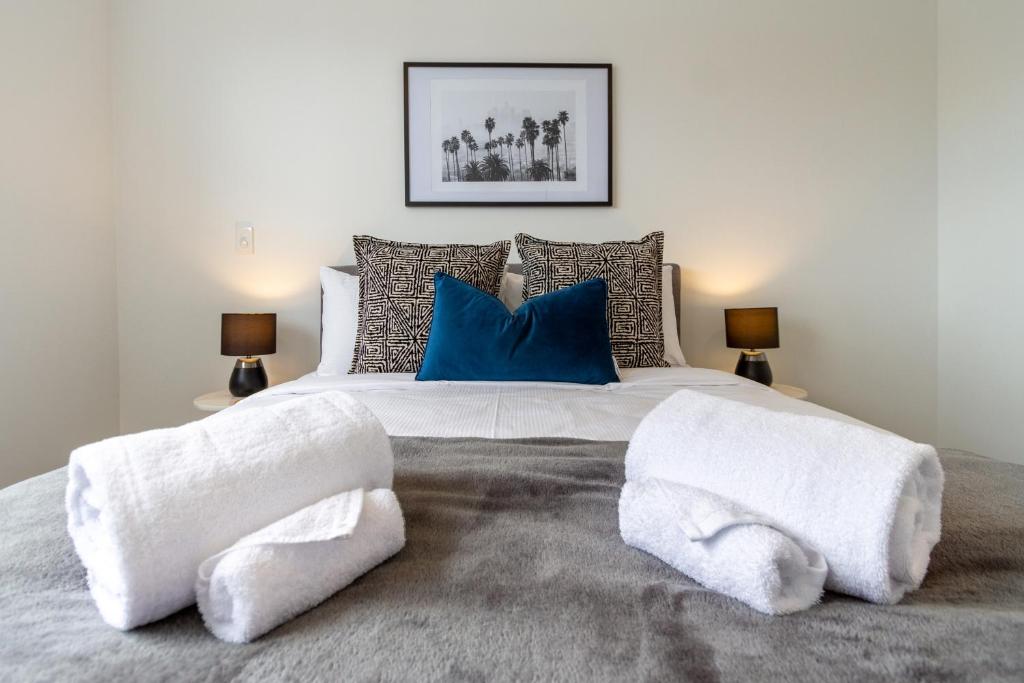 een groot bed met witte dekens en blauwe kussens bij Upper Riccarton dream - 2 bed 2 bath w/carpark in Christchurch