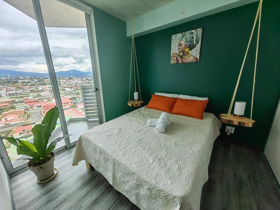 1 dormitorio con paredes verdes y 1 cama con almohadas de color naranja en 1515 SECRT Sabana Hermoso Apartamento Totalmente Equipado, en San José