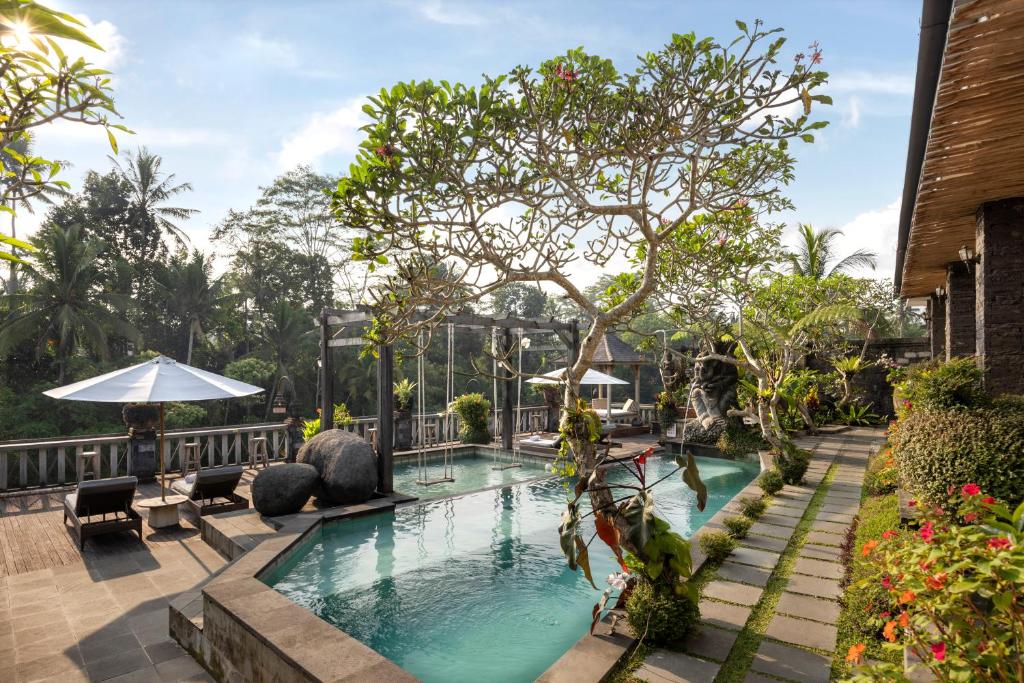 a swimming pool at a resort with a tree at Kawi Resort Ubud in Tegalalang