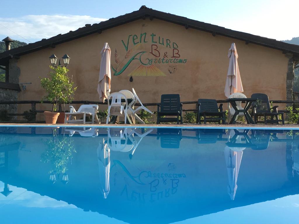 a swimming pool with chairs and umbrellas in front of a building at Venturo Agriturismo Restaurant & Horses in Castelnuovo di Garfagnana