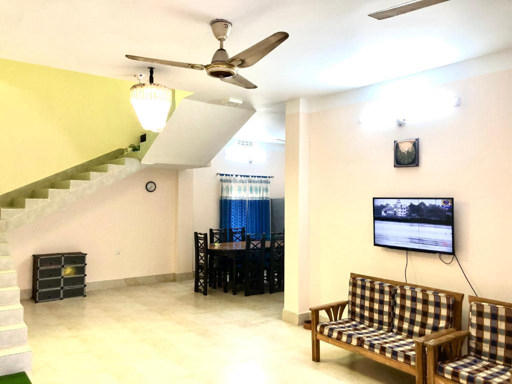 a living room with a couch and a tv on the wall at Pirojpur Guest House 
