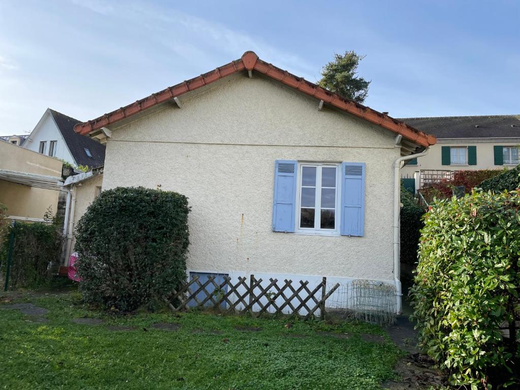 ein weißes Haus mit einem blauen Fenster und einem Zaun in der Unterkunft Le Chalet in Saint-Germain-en-Laye