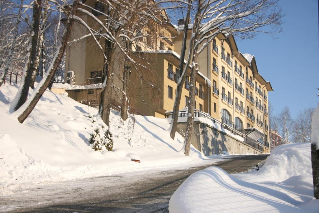 Large multi-story hotel building on a snowy slope, leafless trees and clear blue winter sky