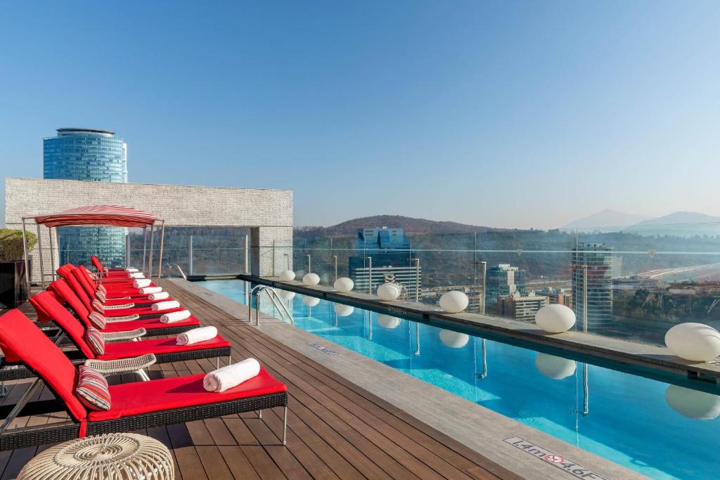 a swimming pool with red lounge chairs on the roof of a building at W Santiago in Santiago