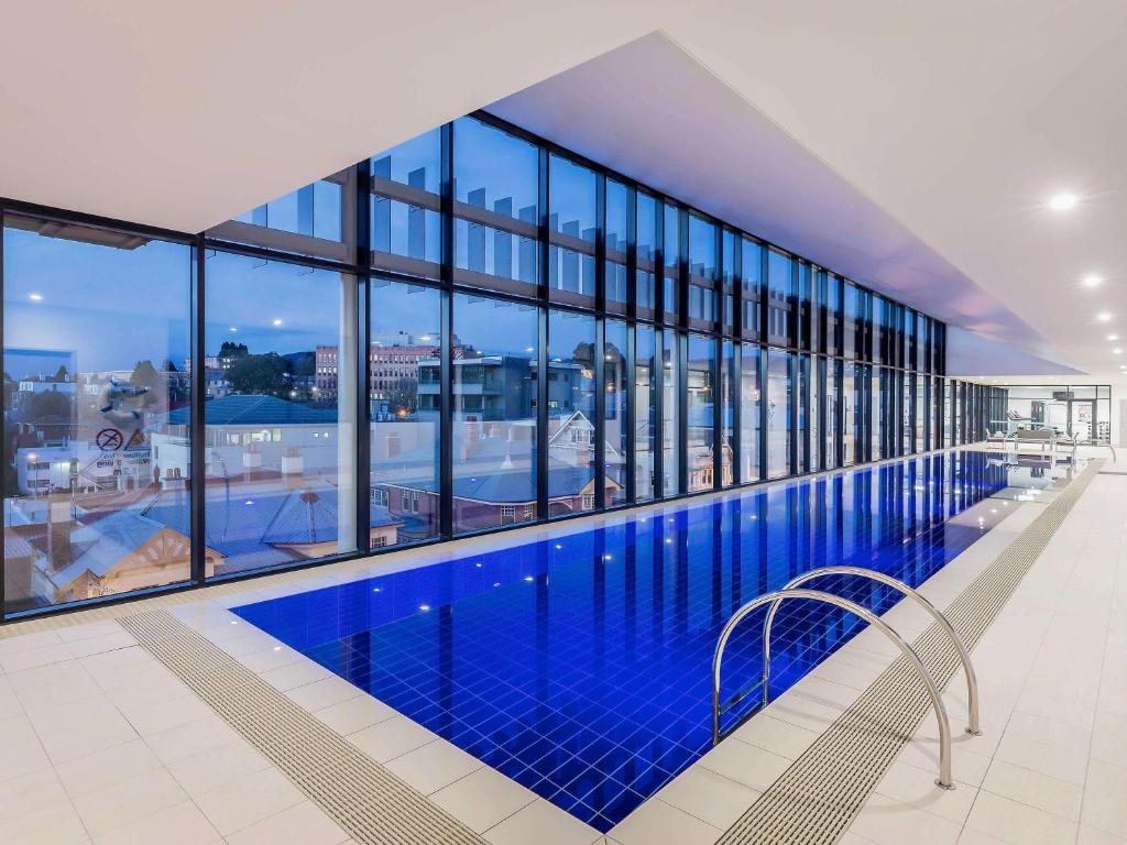 a large swimming pool in a building with windows at Ibis Styles Hobart in Hobart