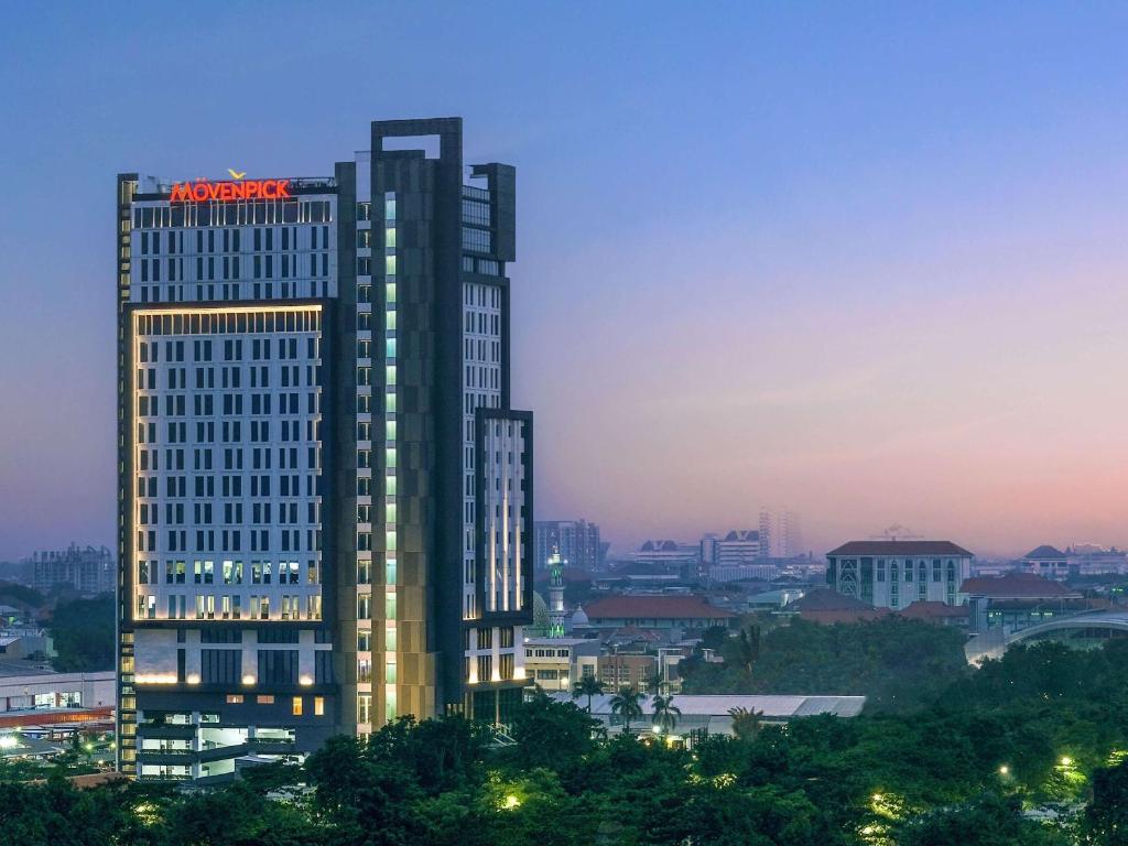 um edifício alto com um letreiro de néon em cima em Movenpick Surabaya City em Surabaia