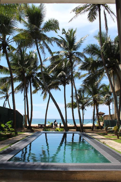una piscina con palmeras y el océano en Guli Beach Hotel, en Hikkaduwa