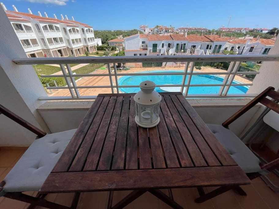 a wooden table on a balcony with a view of a pool at Galdana Apartamento con piscina in Cala en Blanes