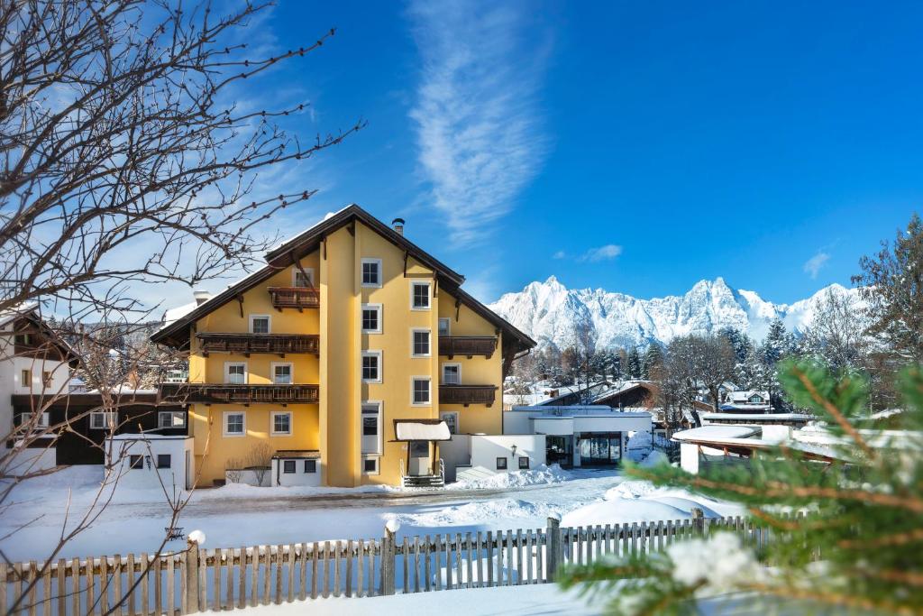 ein gelbes Apartmenthaus mit verschneiten Bergen im Hintergrund in der Unterkunft Alpenhof in Seefeld in Tirol