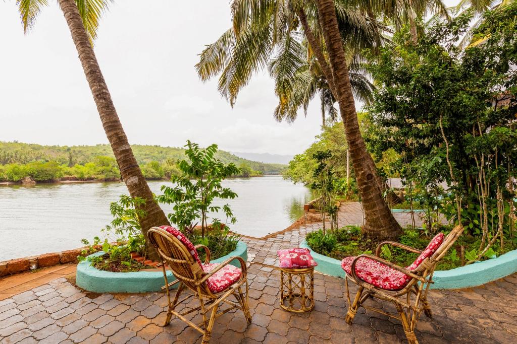 a patio with two chairs and a table and palm trees at Angels River Villa in Canacona