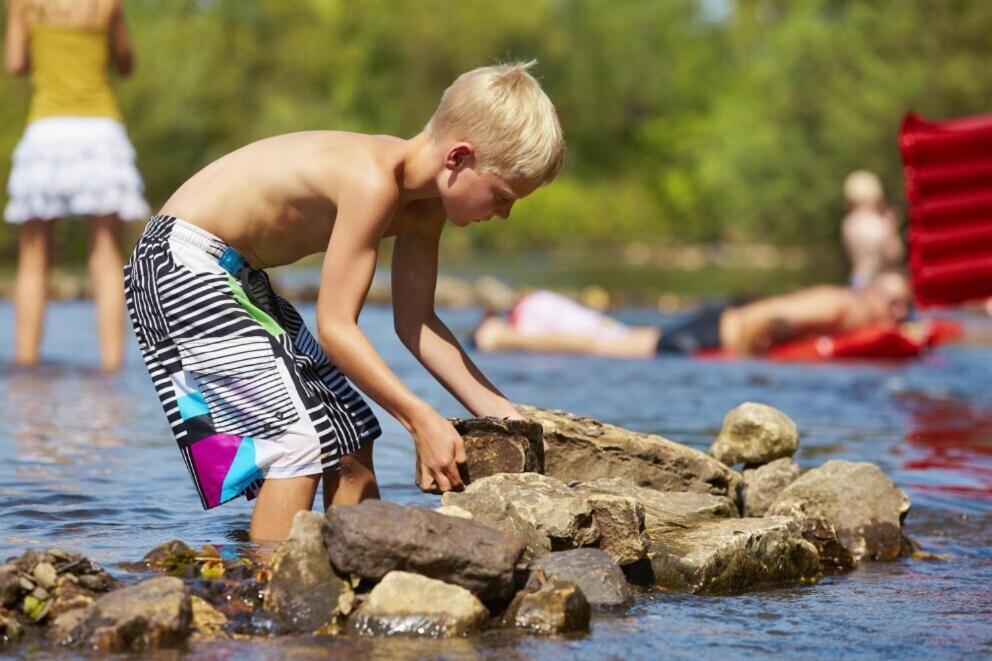 a young boy playing with rocks in the water at Camping De Chênefleur in Tintigny