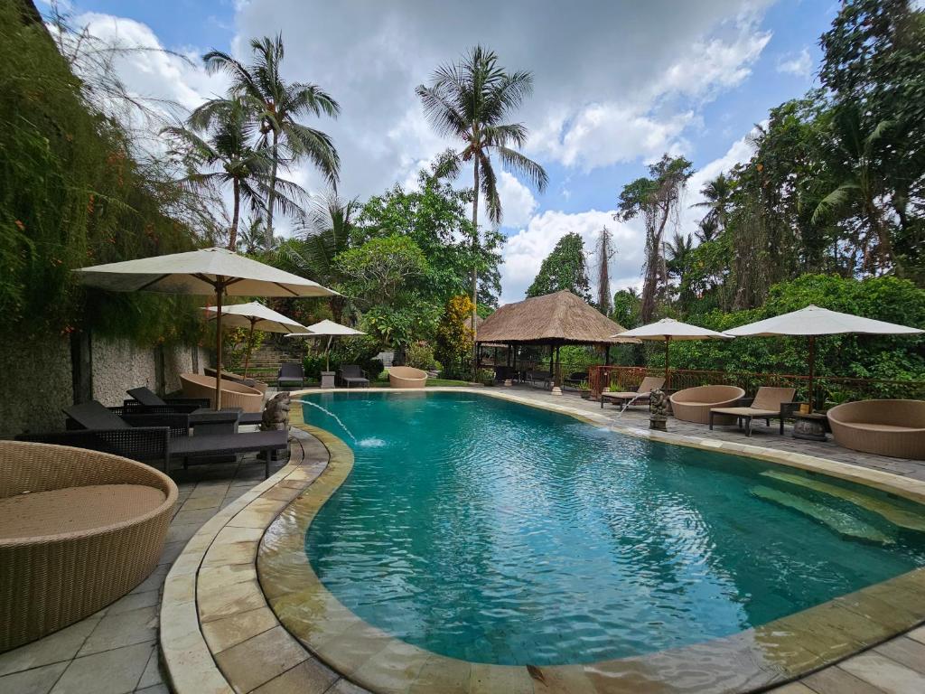 uma piscina com mesas, cadeiras e guarda-sóis em The Gana Ubud by Guru experience em Ubud