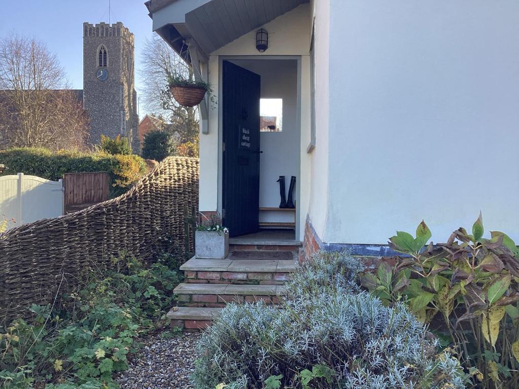 a white house with a blue door and a fence at Black Sheep Cottage in Saxmundham