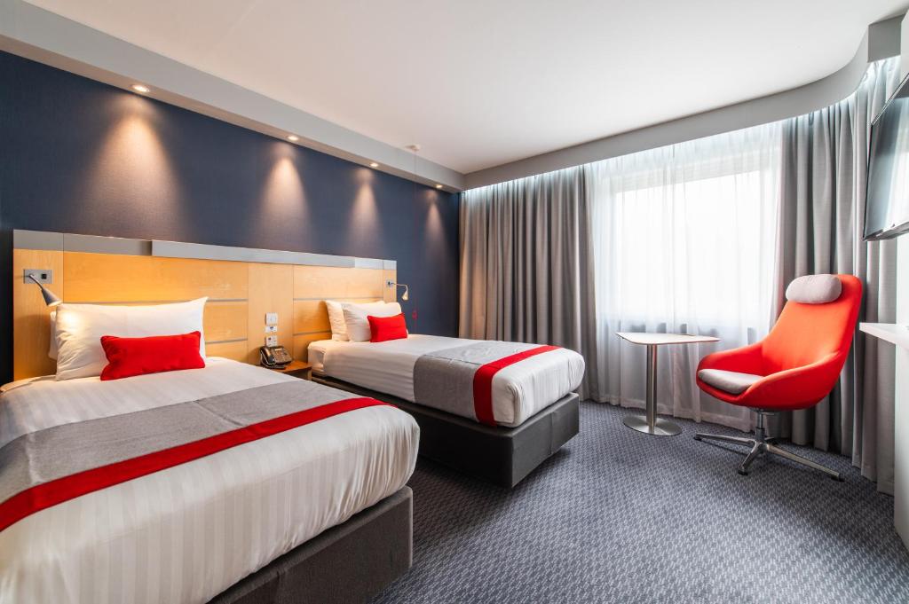 a hotel room with two beds and a red chair at Holiday Inn Express Ramsgate – Minster by IHG in Minster
