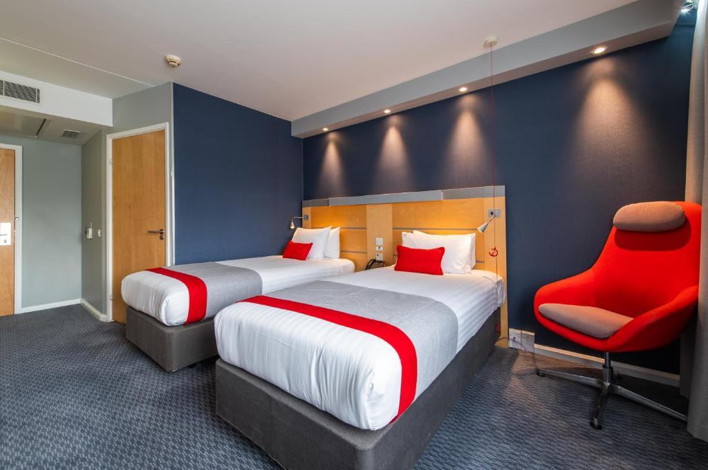a hotel room with two beds and a red chair at Holiday Inn Express Ramsgate – Minster by IHG in Minster