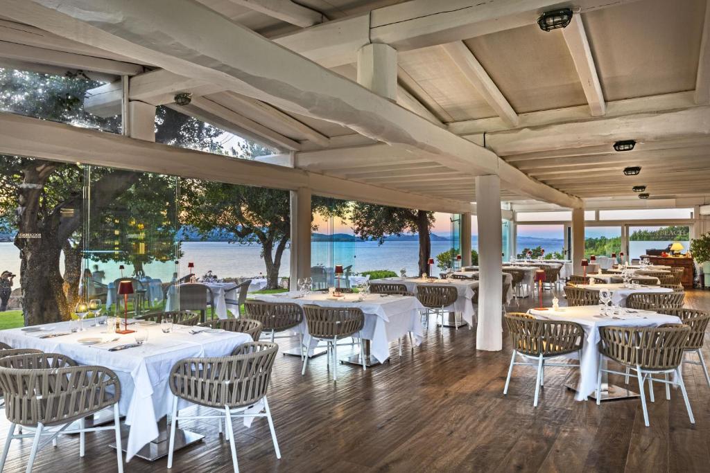 un restaurante con mesas y sillas blancas y el océano en Hotel La Rocca Resort & Spa, en Baja Sardinia