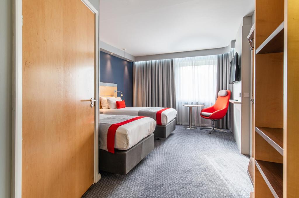 a hotel room with two beds and a red chair at Holiday Inn Express Ramsgate – Minster by IHG in Minster