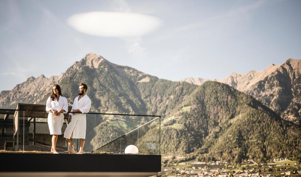 a man and woman standing on top of a building with mountains at Vinea - Suites in Tirolo