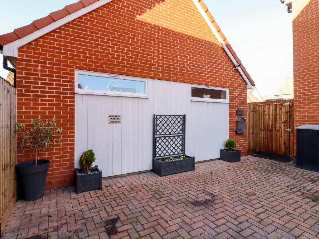 a white garage with potted plants in front of a brick building at Little Haven in Frinton-on-Sea