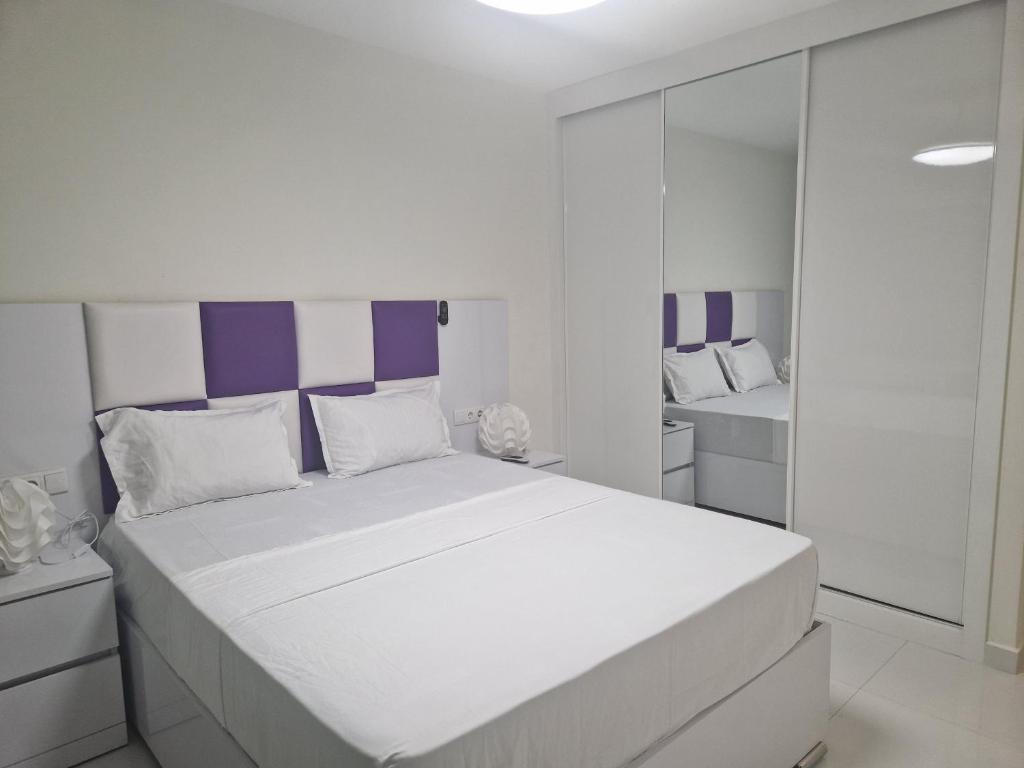 a white bedroom with a large bed and a mirror at SUITES-HOME, CIDADELA in Praia
