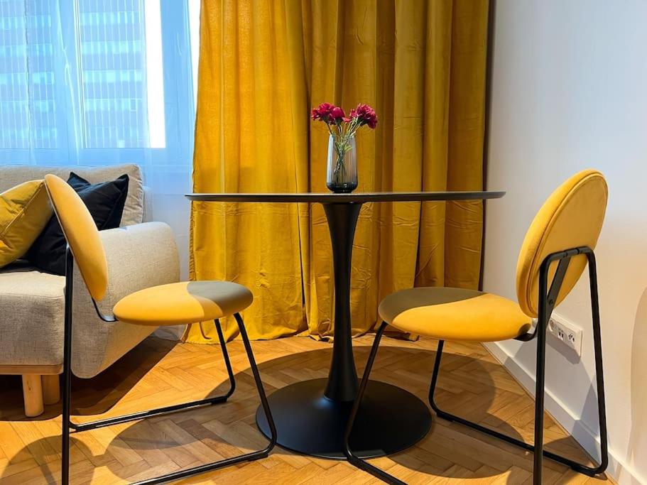 a table with yellow chairs and a vase with flowers at Central Getaway studio in Bratislava