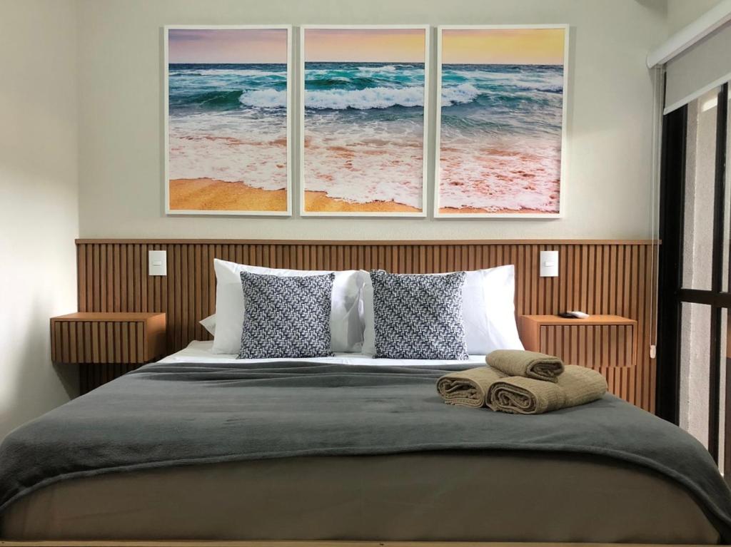 a bedroom with a bed with three paintings on the wall at Flat em Juquehy in São Sebastião