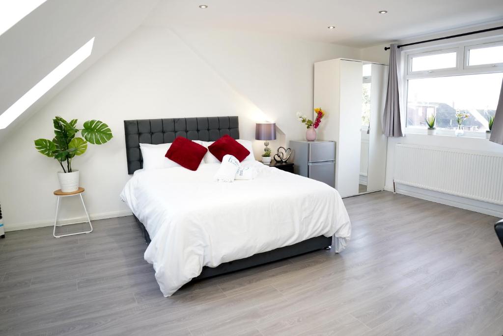 a white bedroom with a large bed with red pillows at 32GC Dreams Unlimited - Heathrow Studio Flat w free on-street parking in Staines upon Thames