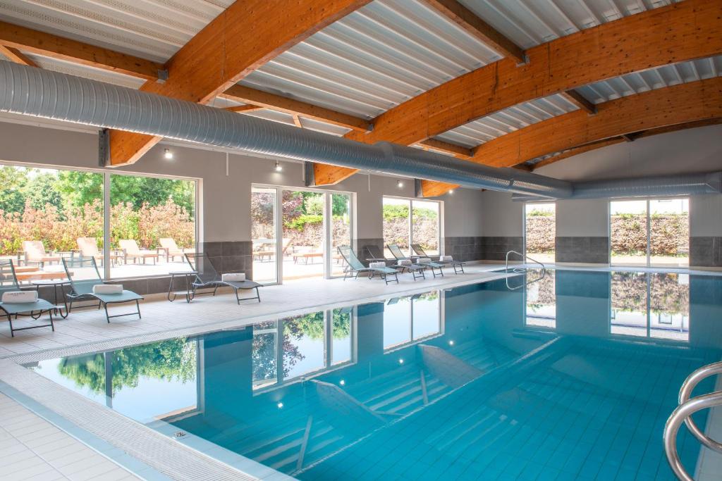 - une piscine avec des chaises et des tables dans un bâtiment dans l'établissement Golden Tulip Dieppe Hôtel & Spa, à Saint-Aubin-sur-Scie