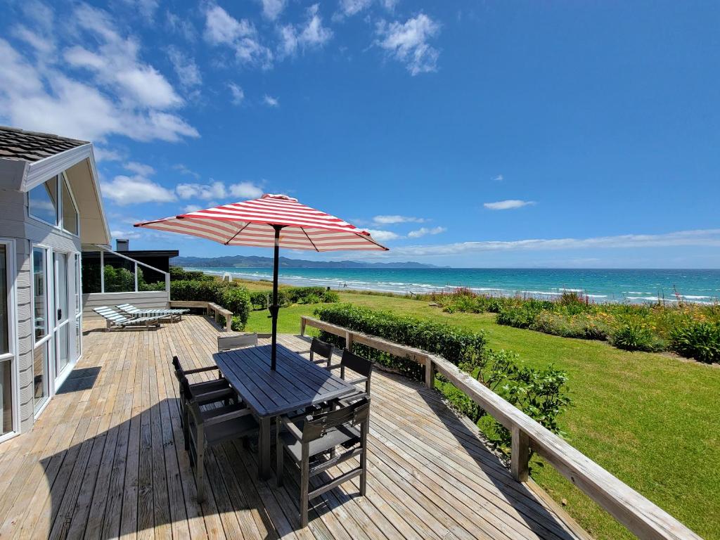 una terraza de madera con mesa y sombrilla en Matarangi Beachfront - Matarangi Holiday Home, en Matarangi