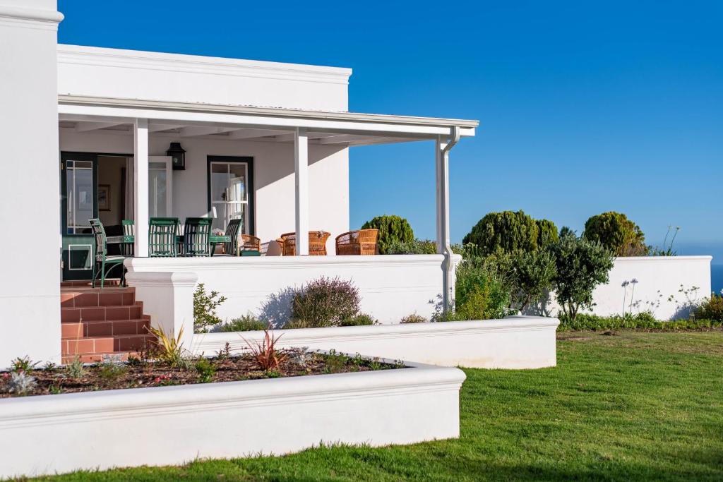 ein weißes Haus mit einer Veranda und Gras in der Unterkunft Greenhill Farm Parklands Cottage - 2 bedroom 4 guests - Private House in Plettenberg Bay