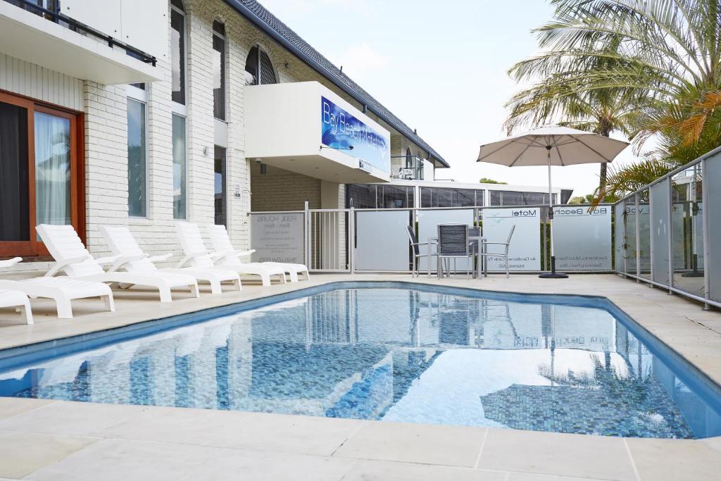 - une piscine avec des chaises blanches et un parasol dans l'établissement Bay Beach Motel, à Byron Bay