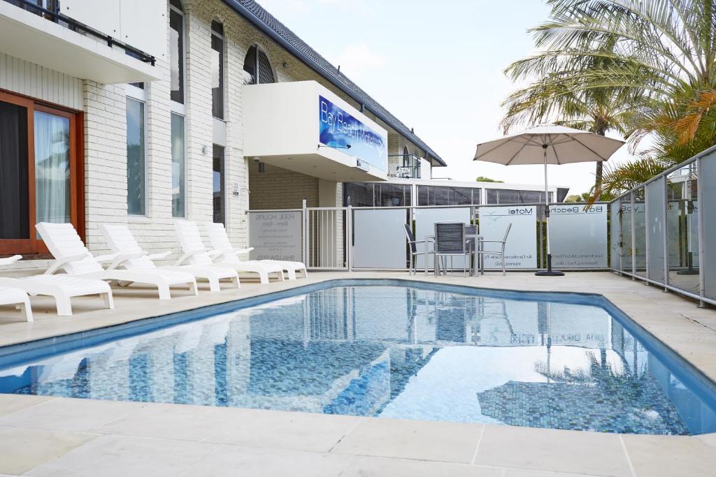 a swimming pool with white chairs and an umbrella at Bay Beach Motel in Byron Bay