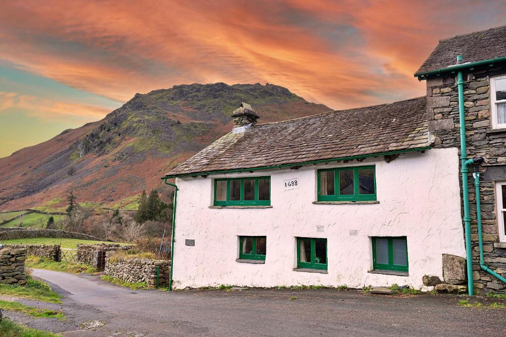 a white house with green windows in front of a mountain at Finest Retreats - No 2 Town Head Cottages in Grasmere
