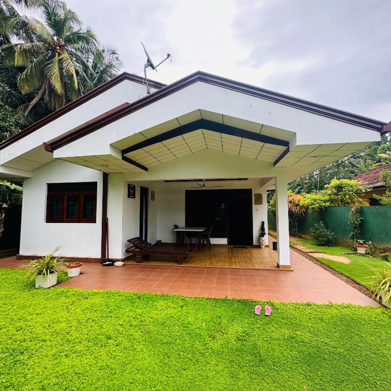 a white house with a patio and grass at Jimmy House in Aluthgama