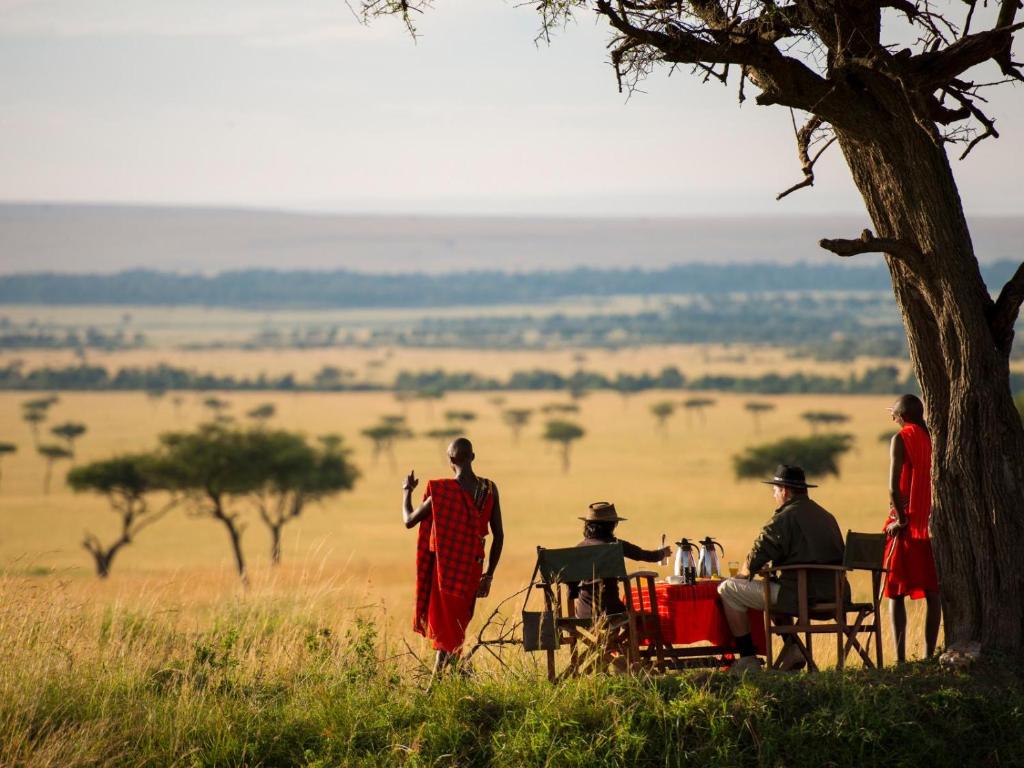 a group of people standing around a table in a field at Kilima Camp - Safari in Masai Mara in Lolgorien