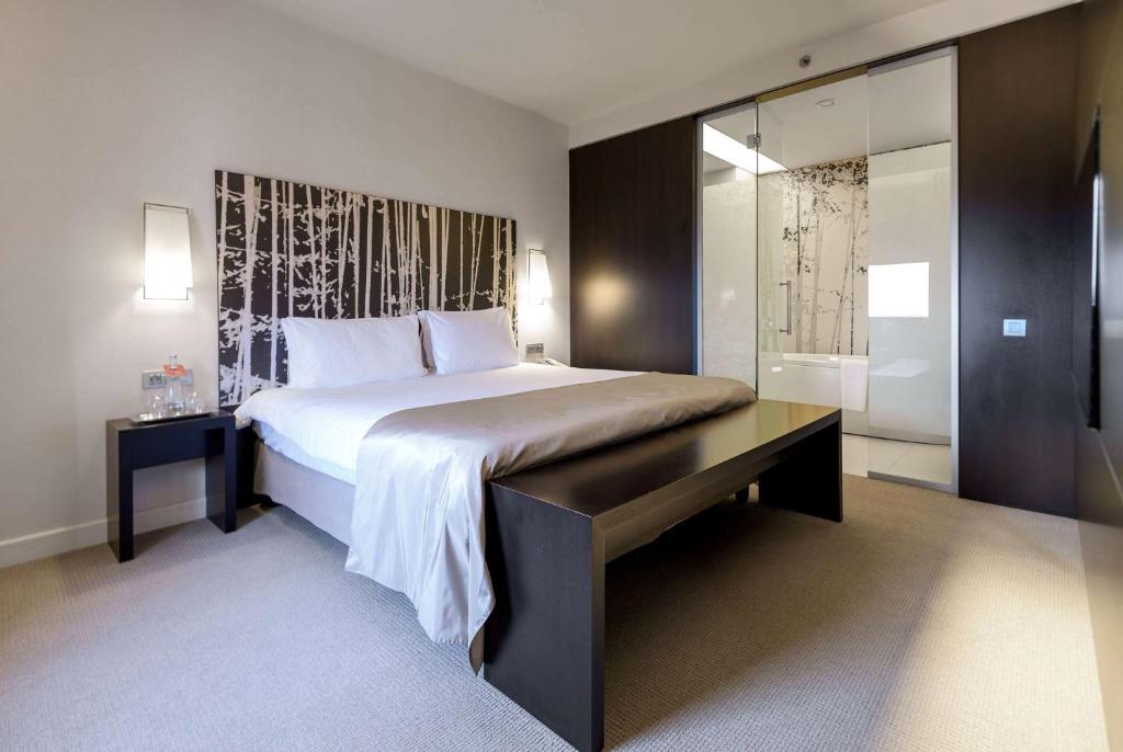 a bedroom with a bed with a desk and a bathroom at Ramada Plaza by Wyndham Bucharest Convention Center in Bucharest