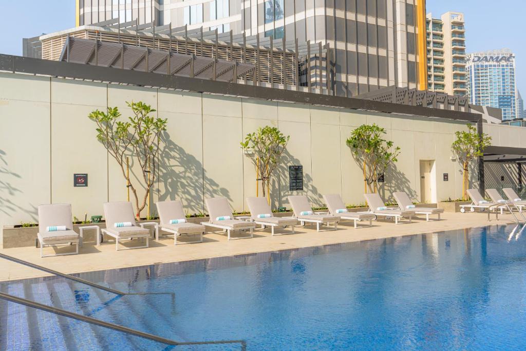 Holiday Inn Dubai Business Bay, an IHG Hotel في دبي: مسبح وكراسي صالة بيضاء بجانب مبنى