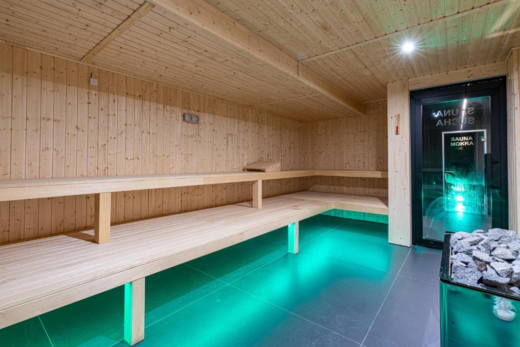 Wood-paneled sauna with tiered wooden benches, heated stone stove and green ambient floor lighting.