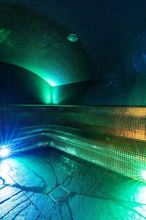 Moody mosaic steam room with curved bench and green-blue atmospheric LED lighting.