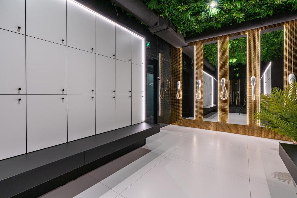 Spa locker room with white lockers, bench, mirrored wall and hanging hairdryers beneath green ceiling.