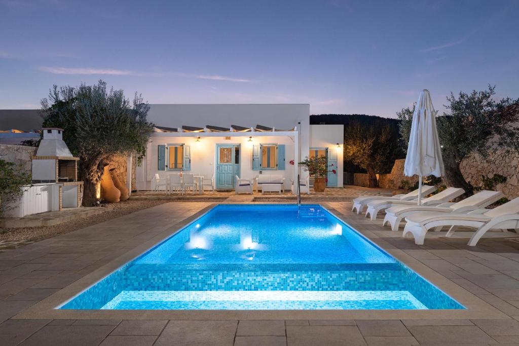 a swimming pool with white chairs and a house at Kalathos Dream Villas in Kalathos