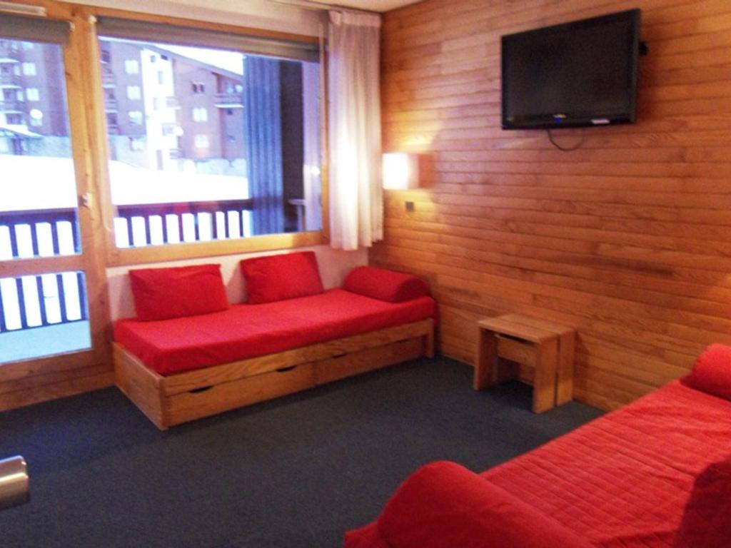 Cette chambre dispose d'un canapé rouge et d'une télévision à écran plat. dans l'établissement Appartement tout confort, accès direct aux pistes, balcon, casier à ski - FR-1-181-2152, à La Plagne Tarentaise