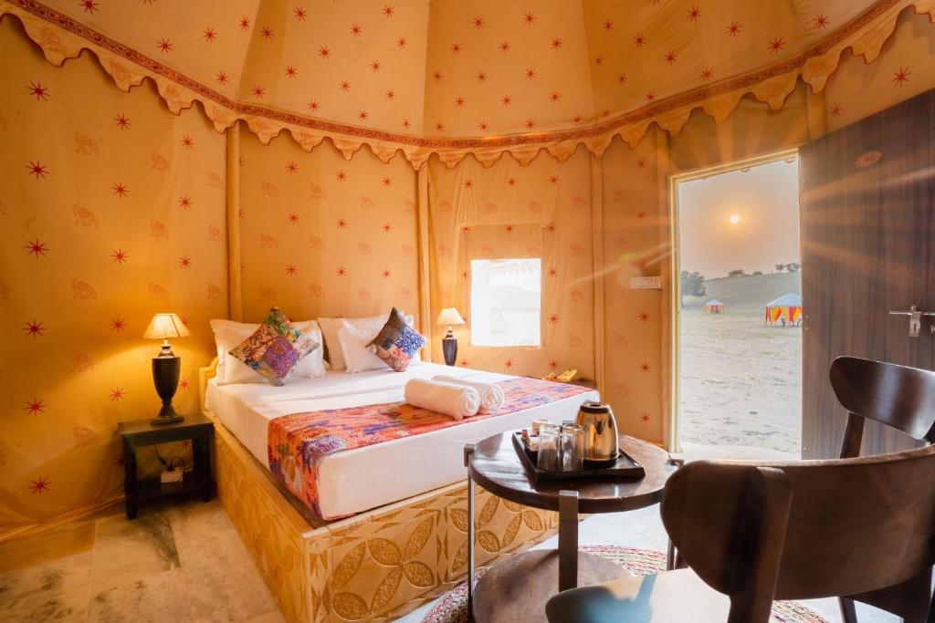 Sonal Desert Camp Jaisalmer في جيلسامر: غرفة نوم بسرير وطاولة في غرفة