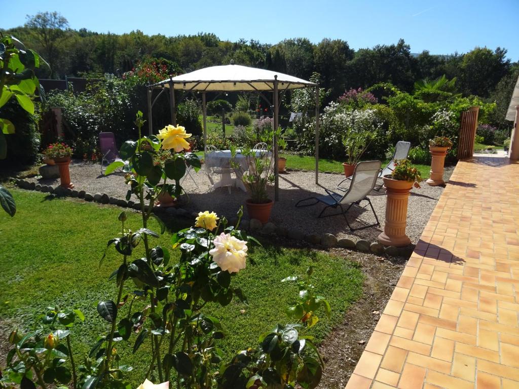 a garden with a table and an umbrella and flowers at Le Clos Fleuri in Caumont