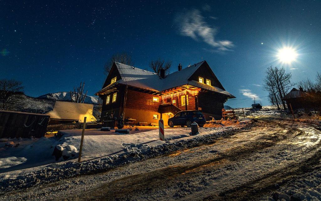 een huis met de lichten aan in de sneeuw bij Drevenica Spiaci Goral in Ždiar
