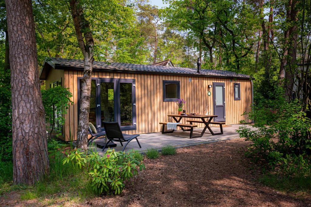 een hut in het bos met een picknicktafel en stoelen bij Lodge Steltloper Nunspeet Veluwe in Nunspeet